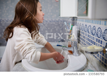 Girl Washing Hands At Sink In Bathroom With Blue Tile Pattern And Mirror Girl Washing Hands At Sink In Bathroom With Blue Tile Pattern And Mirror 133580793