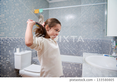 Young Girl Brushing Hair in Bathroom Mirror During Morning Routine at Home Young Girl Brushing Hair in Bathroom Mirror During Morning Routine at Home 133580805