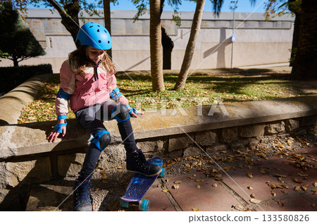Young Girl Skateboarding Outdoors With Helmet And Protective Gear On A Sunny Day Young Girl Skateboarding Outdoors With Helmet And Protective Gear On A Sunny Day 133580826