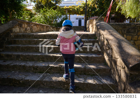 Young Child With Helmet Climbing Stone Steps Carrying Skateboard Outdoors 133580831