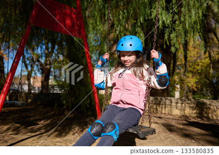 Young Girl On Swing Set Wearing Helmet Enjoys Outdoor Park Play And Fresh Air Young Girl On Swing Set Wearing Helmet Enjoys Outdoor Park Play And Fresh Air 133580835