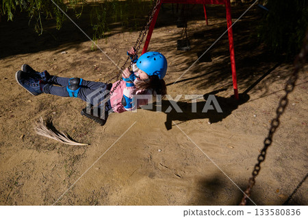 Child Wearing Blue Helmet Swinging on a Playground Swing Set Outdoors Child Wearing Blue Helmet Swinging on a Playground Swing Set Outdoors 133580836