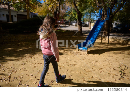 Girl Walking Toward Blue Playground Slide in Autumn Park 133580844