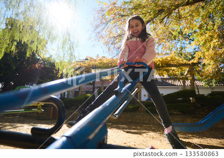 Joyful Child Laughing While Playing on a Blue See-Saw in a Sunny Park Joyful Child Laughing While Playing on a Blue See-Saw in a Sunny Park 133580863