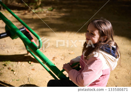 Girl On Playground Seesaw Smiling While Sitting On Green Metal Seesaw 133580871