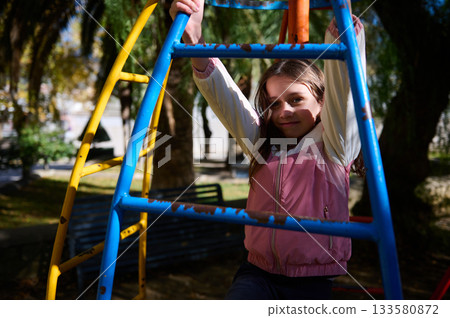 Young Girl On Colorful Playground Equipment Enjoying Outdoor Playtime In Bright Sunlight 133580872