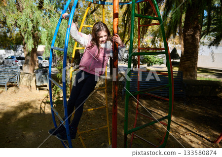 Girl Plays On Colorful Jungle Gym In Park, Outdoor Playground Fun And Adventure Girl Plays On Colorful Jungle Gym In Park, Outdoor Playground Fun And Adventure 133580874