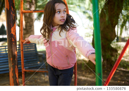 Young Girl Exploring Playground Climbing Frame In Pink Jacket On A Sunny Day Young Girl Exploring Playground Climbing Frame In Pink Jacket On A Sunny Day 133580876