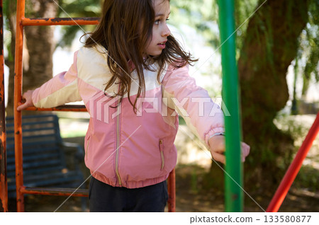 Girl At Playground In Pink Jacket Reaching On Colorful Metal Bars Girl At Playground In Pink Jacket Reaching On Colorful Metal Bars 133580877