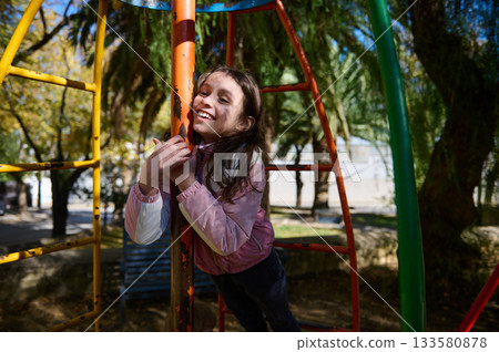 Joyful Girl Climbs Colorful Playground Structure on a Sunny Day at the Park Joyful Girl Climbs Colorful Playground Structure on a Sunny Day at the Park 133580878