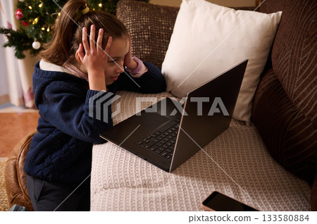 Young Girl Frustrated At Laptop On Couch By Christmas Tree During Holiday Young Girl Frustrated At Laptop On Couch By Christmas Tree During Holiday 133580884