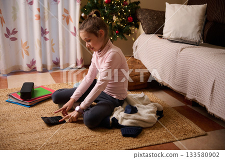 Girl Learns At Home With Calculator And Notebooks Near Christmas Tree 133580902