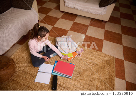Child Sitting On Rug Doing Homework With Notebooks And Plush Toy In Living Room 133580910