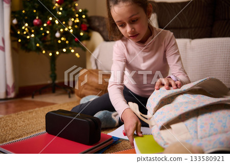 Young Girl Studying At Home With Backpack And Christmas Tree In Cozy Living Room 133580921