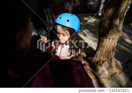 Girl With Blue Helmet Getting Ready For Outdoor Adventure With Help From Adult 133581023