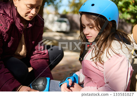 Young Girl in Blue Bike Helmet Receives Help Outdoors During Family Activity 133581027