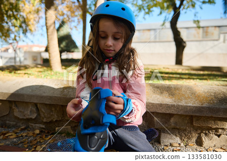 Young Girl In Pink Jacket Plays With Blue Roller Skates While Wearing A Helmet Young Girl In Pink Jacket Plays With Blue Roller Skates While Wearing A Helmet 133581030