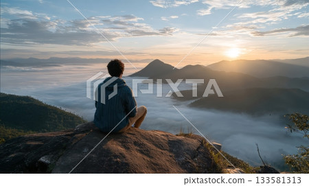 A solo traveler sits on a rock, admiring stunning mountains bathed in the soft light of a winter sunrise A solo traveler sits on a rock, admiring stunning mountains bathed in the soft light of a winter sunrise 133581313