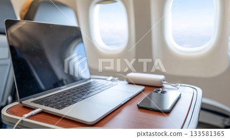 Laptop and smartphone on a tray table in an airplane, showcasing remote work setup with power bank Laptop and smartphone on a tray table in an airplane, showcasing remote work setup with power bank 133581365