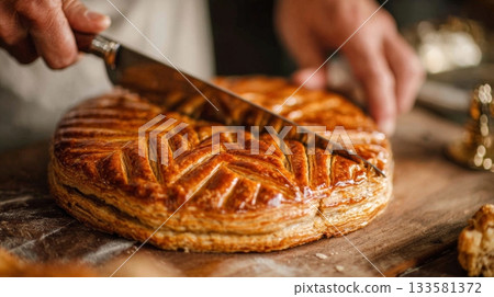Close up of hand cutting French Galette des Rois, showcasing flaky pastry texture and festive atmosphere for Three Kings Day celebration 133581372