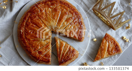French Galette des Rois dessert on a white plate with a golden crown, showcasing a festive Three Kings Day celebration 133581374