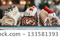Three distinct styles of buche de noel arranged elegantly on a glass display table with luxurious patisserie lighting 133581393