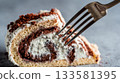 Macro photo of a fork piercing the creamy swirl of a buche de noel slice, showcasing rich textures and warm tones for holiday dessert lovers 133581395