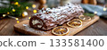 Long buche de noel on wooden board, decorated with dried citrus slices and powdered sugar, surrounded by festive lights and holiday ambiance 133581400
