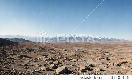 A panorama of a vast, arid region of distant snow-capped mountains and desolate rocky terrain. 133581426