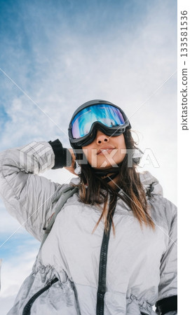 A young woman in a silver puffer jacket poses against a stunning snowy mountain backdrop while enjoying her winter adventure 133581536