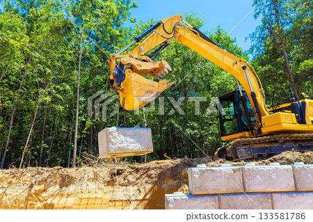 Heavy machinery moves large stone block at busy construction site with for retaining wall 133581786