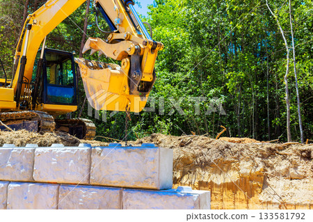 Heavy machinery lifts large blocks at construction site wooded under creating retaining wall Heavy machinery lifts large blocks at construction site wooded under creating retaining wall 133581792