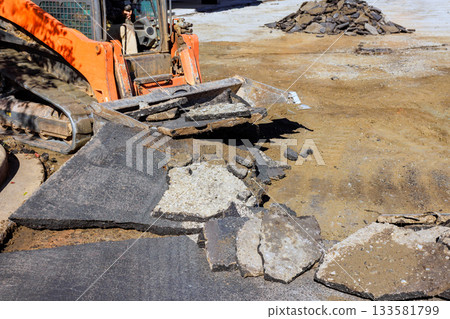 Heavy machinery is breaking up old pavement at construction site while workers prepare for repairs road reconstruction 133581799