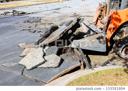 Construction skid steer is clearing debris from damaged pavement during road repair 133581804