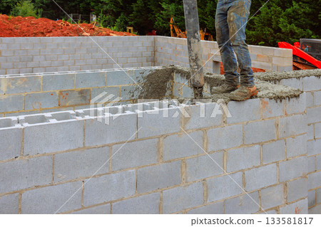 Construction worker is actively pouring concrete into gray block wall using cement pump at construction site 133581817