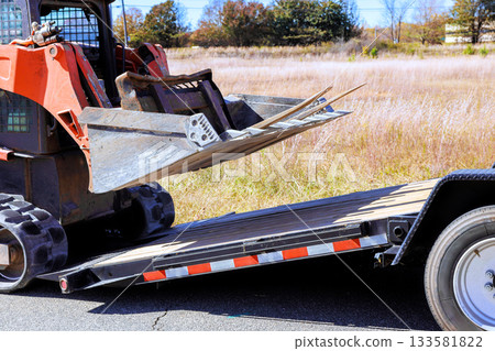 An skid steer is unloading on flatbed trailer at construction site 133581822