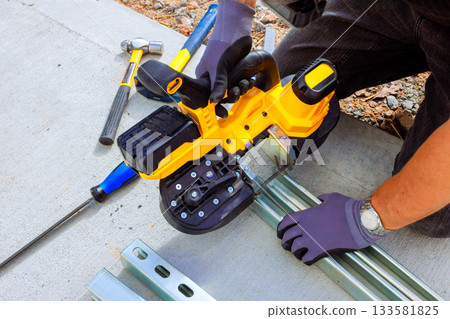 Worker uses an handheld electric saw cutting metal framing while constructing new building 133581825