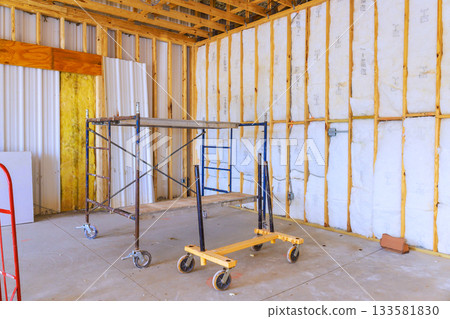 Scaffolding stands in an unfinished room with exposed walls insulation materials on construction work Scaffolding stands in an unfinished room with exposed walls insulation materials on construction work 133581830
