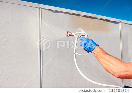 Handyman in gloves uses spray gun to paint wall under works day Handyman in gloves uses spray gun to paint wall under works day 133581834