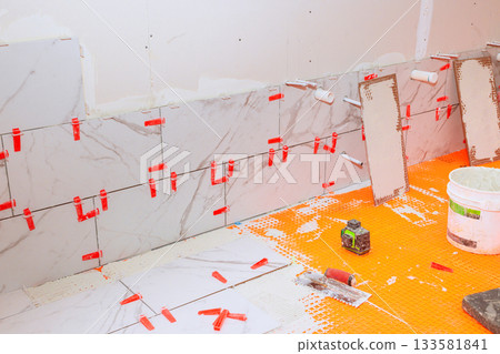 Workers are busy installing large marble tiles on bathroom wall using spacers for even gaps. Workers are busy installing large marble tiles on bathroom wall using spacers for even gaps. 133581841