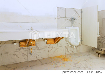 Renovation work is ongoing in bathroom with exposed plumbing unfinished fixtures urinal at wall. 133581852