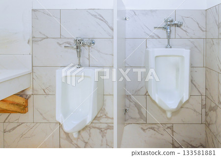 Two modern urinals are placed side by side in tiled restroom with bright lighting simple design. Two modern urinals are placed side by side in tiled restroom with bright lighting simple design. 133581881