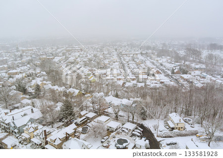 Snowy storm winter morning features neighborhood blanketed in snow, with rooftops trees covered in white snow Snowy storm winter morning features neighborhood blanketed in snow, with rooftops trees covered in white snow 133581928