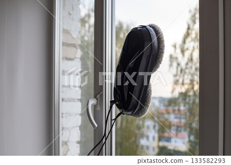 Black robot window cleaner washes a window in city apartment. the cleaning process with modern household appliances. Black robot window cleaner washes a window in city apartment. the cleaning process with modern household appliances. 133582293