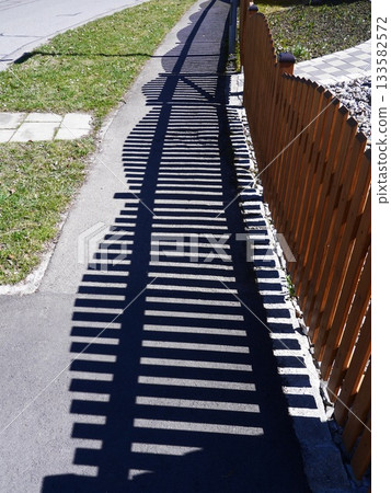 Shadow of a fence is cast on the sidewalk Shadow of a fence is cast on the sidewalk 133582572