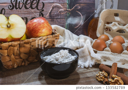 Rustic kitchen scene with fresh preparation of a gourmet dessert with red apples, cinnamon, eggs and nuts. 133582789