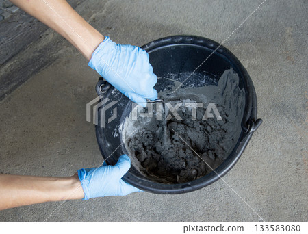 Construction workers are mixing cement in a bucket. 133583080