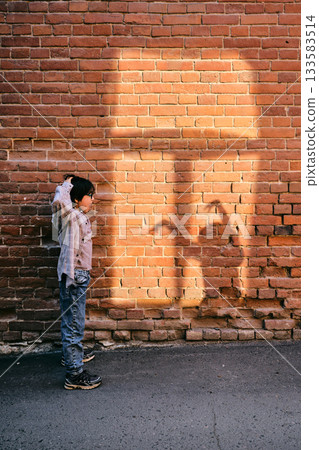 A boy looks at a shadow on the wall in the view of another person in the window A boy looks at a shadow on the wall in the view of another person in the window 133583514