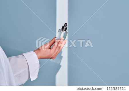 Hand holding skincare serum dropper bottle 133583521