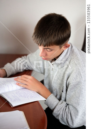 Focused student engaged in studying diligently at a wooden desk in a bright room during the late afternoon, demonstrating the essence of learning and dedication to education 133583961